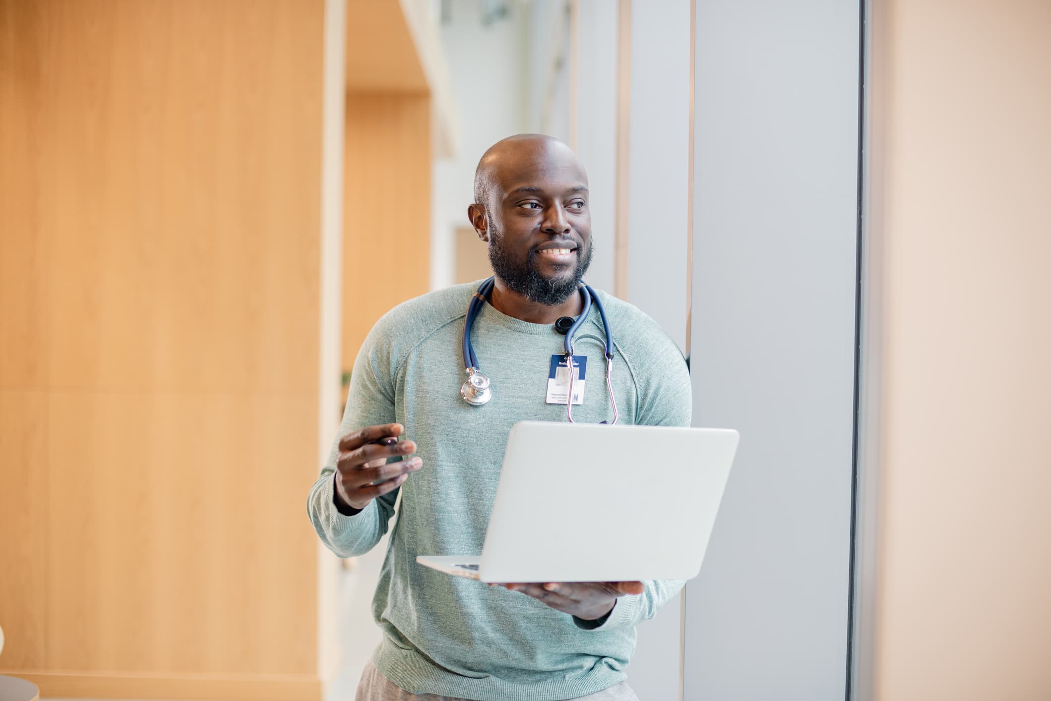 a nurse is holding a laptop whilst looking away from the laptop with a big smile and feeling happy