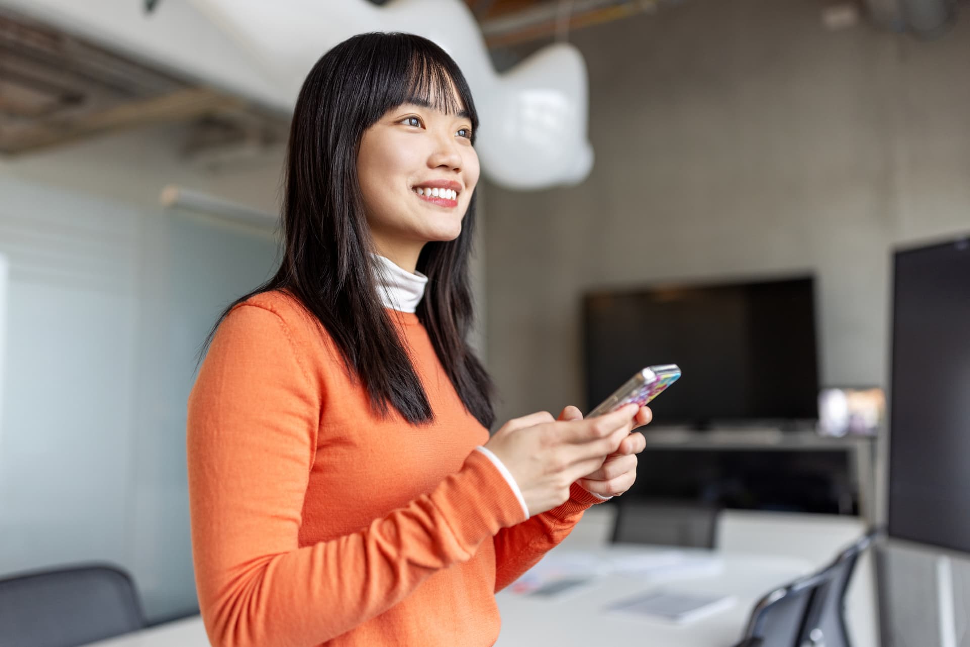 a person using their smartphone, looking away from the phone with a big smile and feeling happy